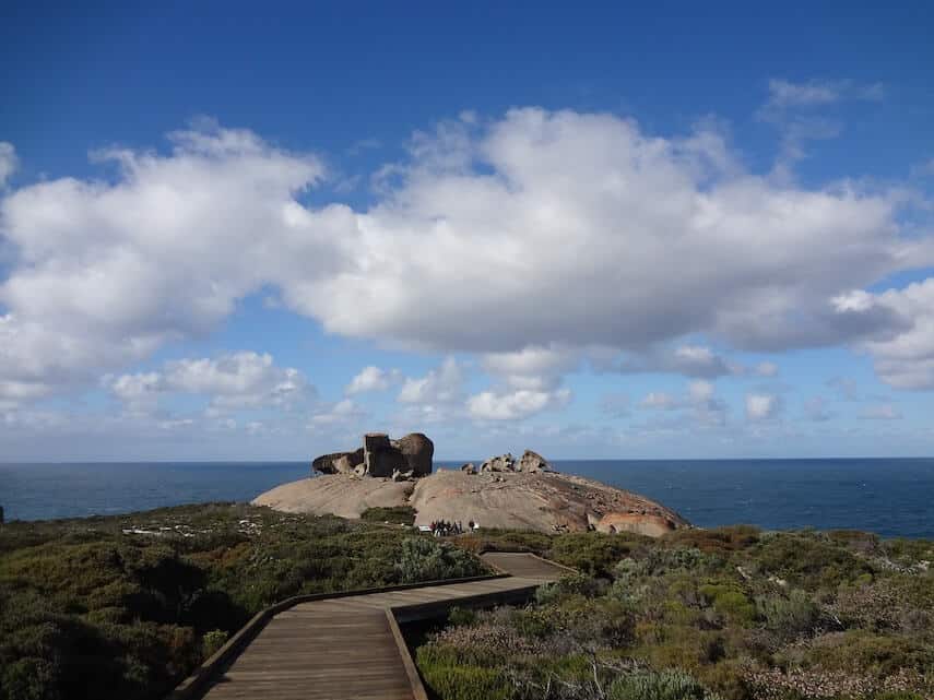 Rocky outcrop with a wooden boardwalk winding through green scrub to get to it with the ocean in the background