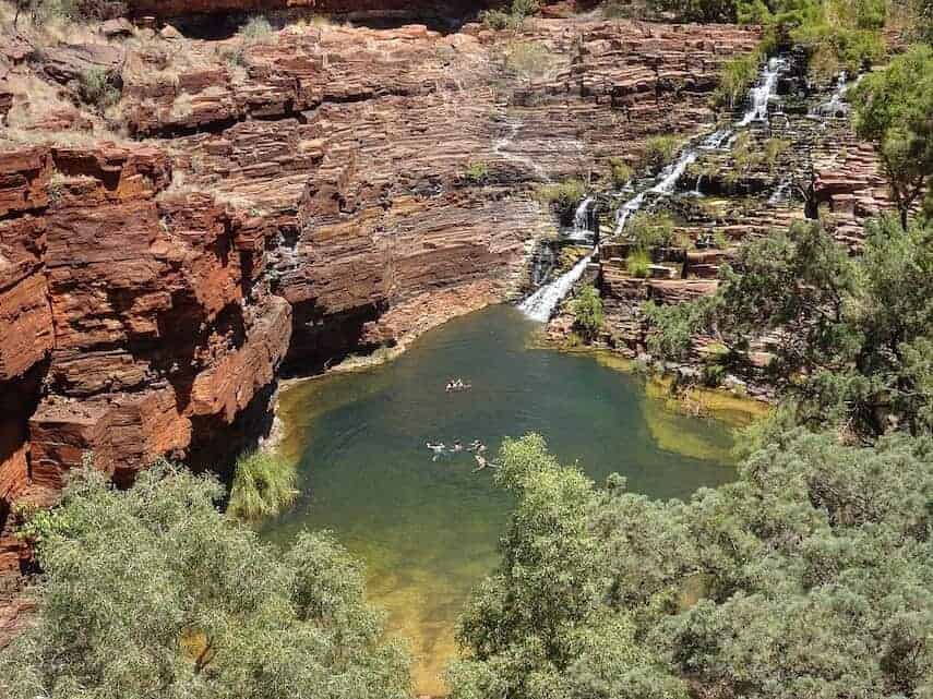 Waterhole with people swimming surrounded by red rock walls in Karijini National Park