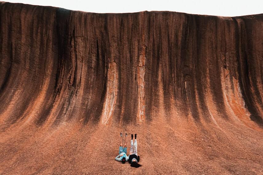 Couple lying at the base of Wave Rock with their feet in the air, WA