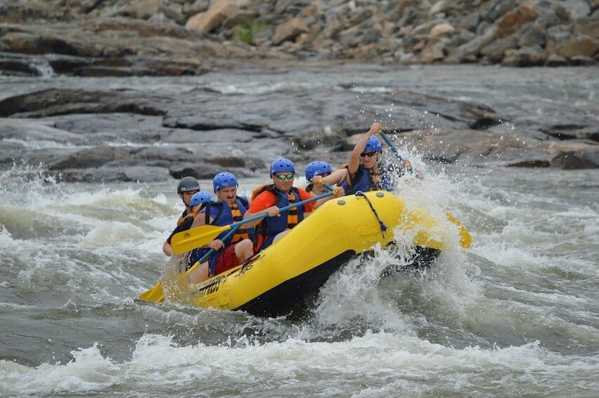 Yellow boat filled with people wearing crash helmets white water rafting