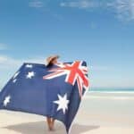 150+ Australian Slang Words & Phrases header image of a woman holding an Australian flag outstretched behind her on the beach wearing a stetson