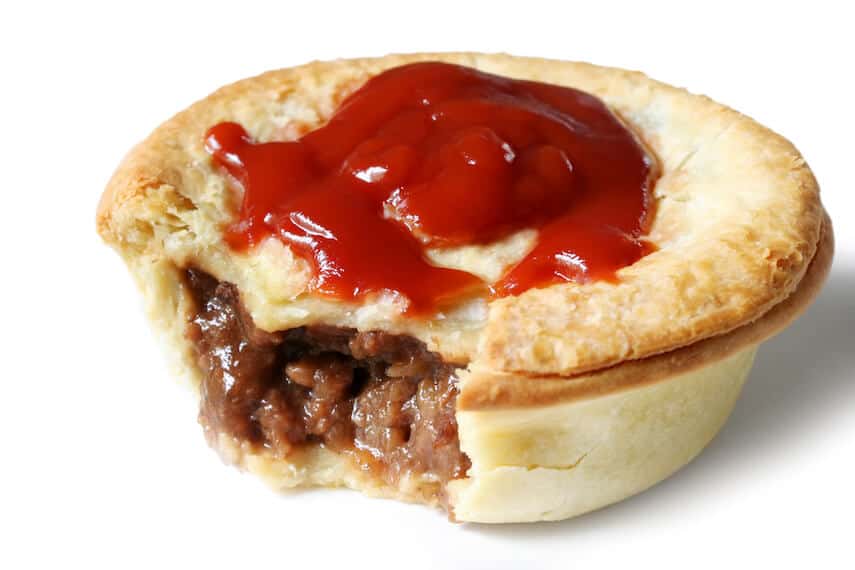 Australian Meat Pie with a bite out of it showing the meat and topped with a splodge of tomato sauce