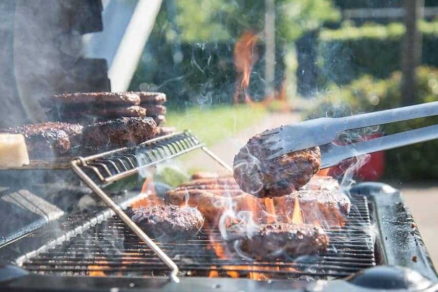 Australian BBQ with top rack with tongs flipping burgers on the bottom