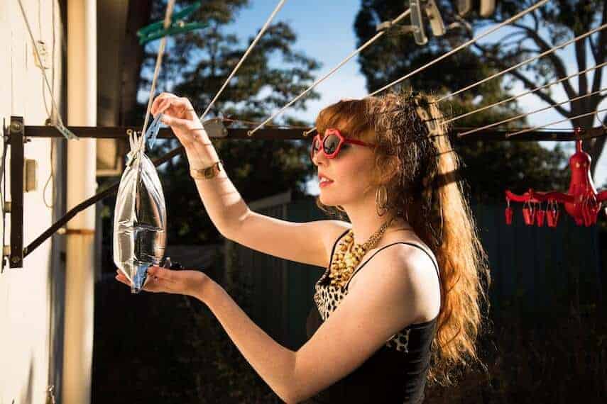 Woman holding a bag of wine (goon) which has been clipped to a washing line