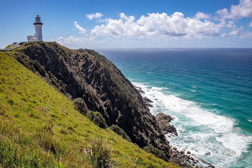 Cape Byron Lighthouse sitting at the top of a rocky outcrop with the ocean below and waves crashing into the rock