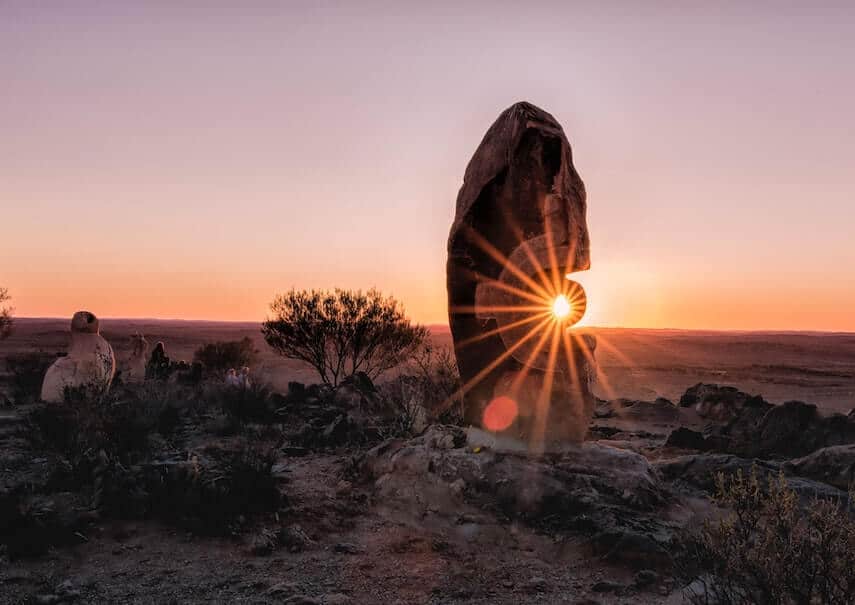 Outback Australia with a rock sculpture framing a sunburst sunset