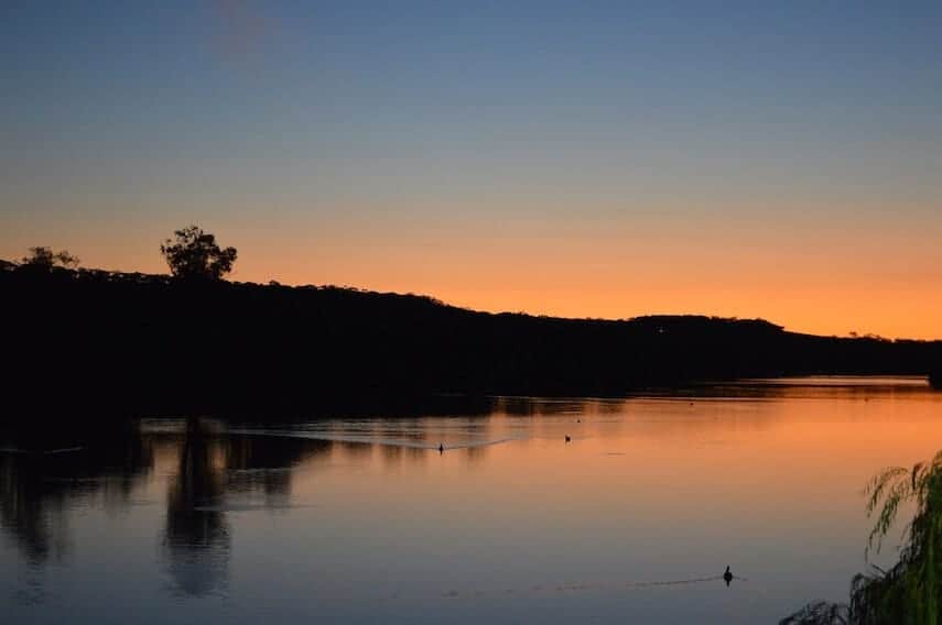 Murray River in NSW at Sunset. The water is flat, the land in the background is in shadow