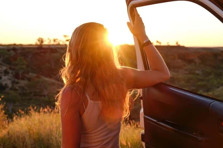 Woman stood next to an open 4x4 car door with her arm on the open window with the sunsetting behind her