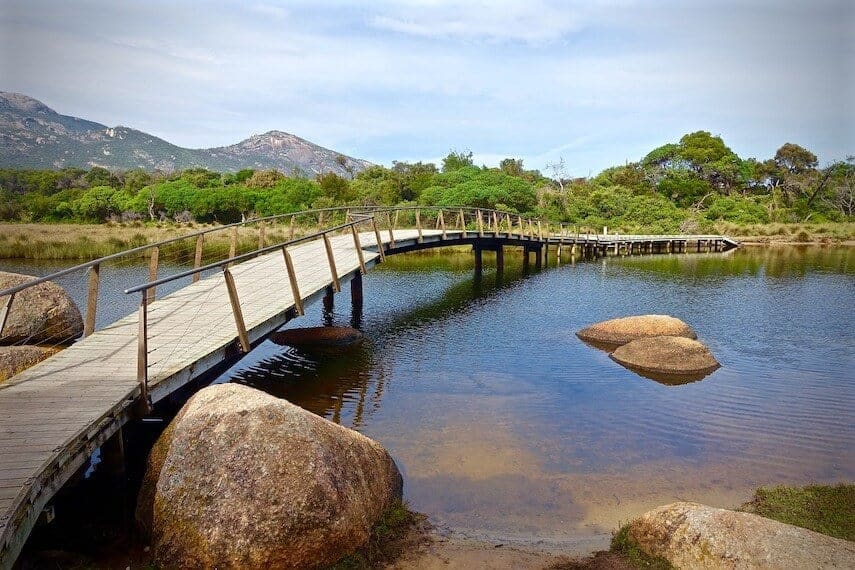 Wooden boardwalk over a tidal river with green trees on the far bank at Wilsons Promontory