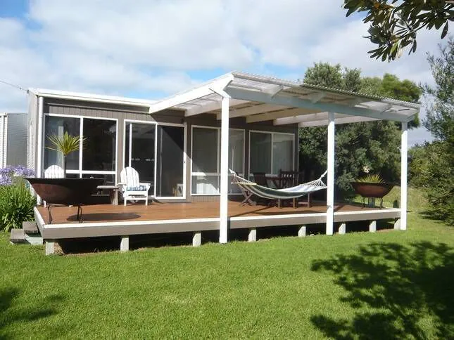 White wooden cabin with covered decking at the back with firepit on the left and hammock on the right