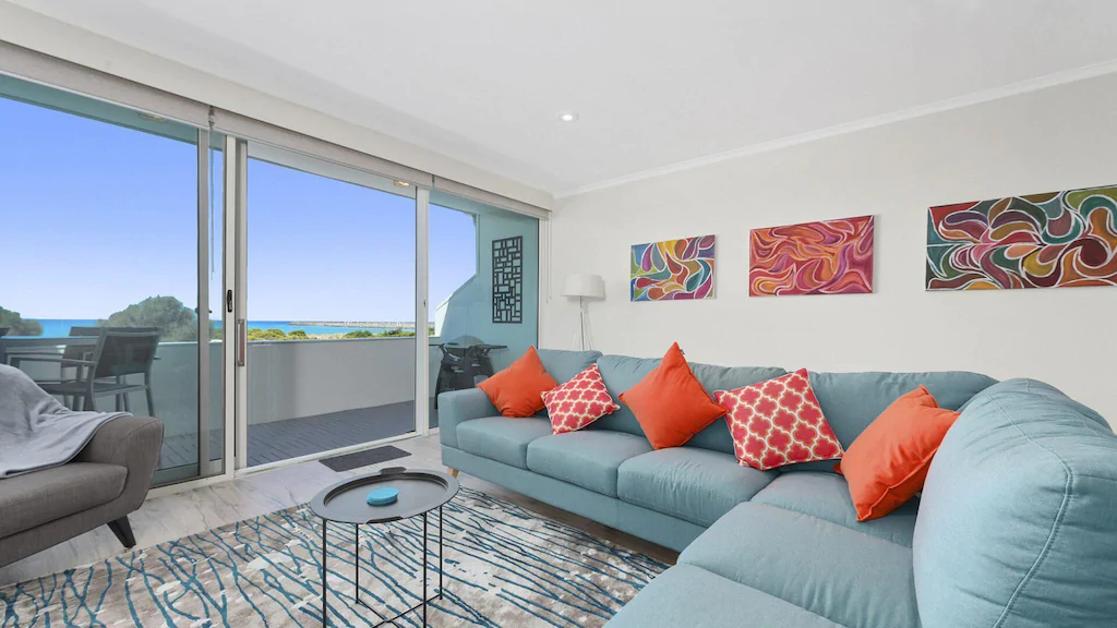 Corner lounge suide next to floor to ceiling windows with red cushions in the Foreshore Apartment