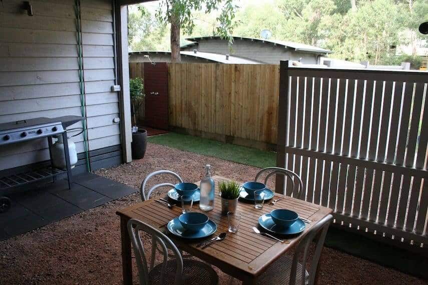 Fenced outdoor area of Lorne Surfdogz with table set for 4 in the foreground and BBQ to the back of shot