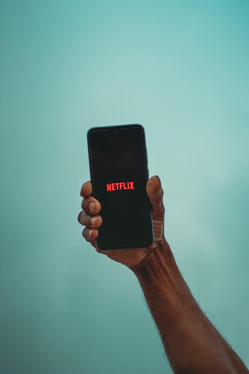 Man holding a phone with the Netflix logo on the screen in front of a green wall