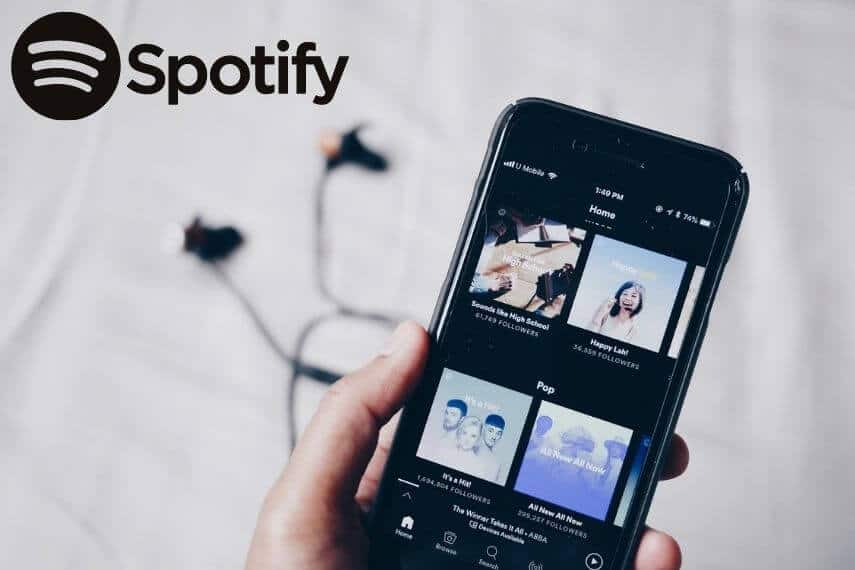 Woman holding a phone with the Spotify App open and headphone dangling on the table below