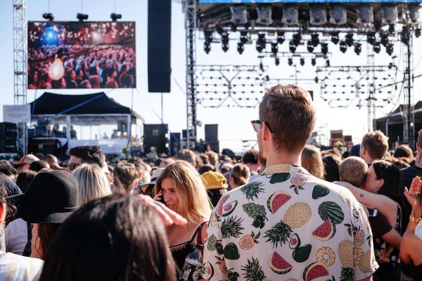 Festival in Melbourne in Spring with a crowd of people standing in front of a stage with lights hung above it