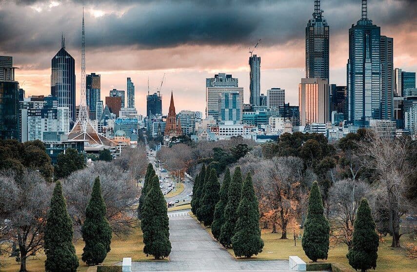 Melbourne skyline as seen from the Shrine of Remembrance looking down a tree tined path under a dark sky