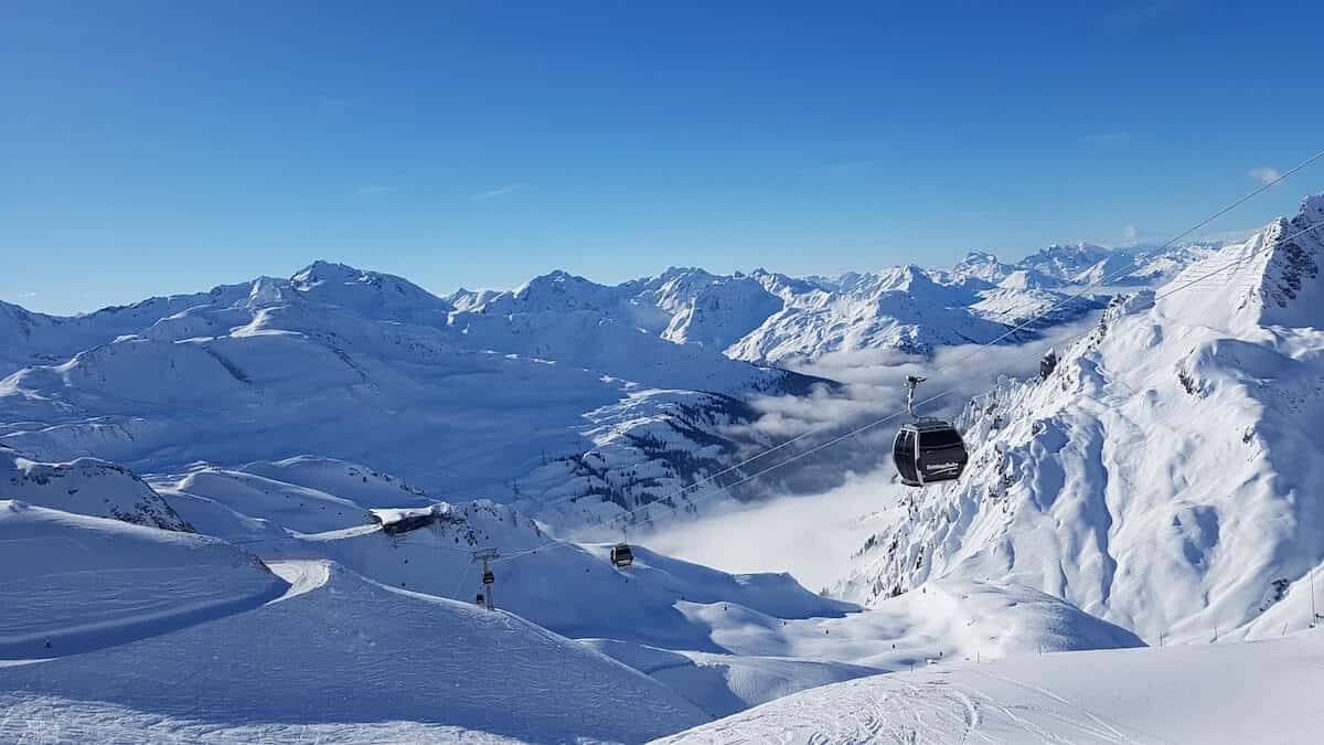 Best Ski Resorts NSW cover photo of snow covered mountains, a gondola lift with black and silver cabins running up the side on the right of the image