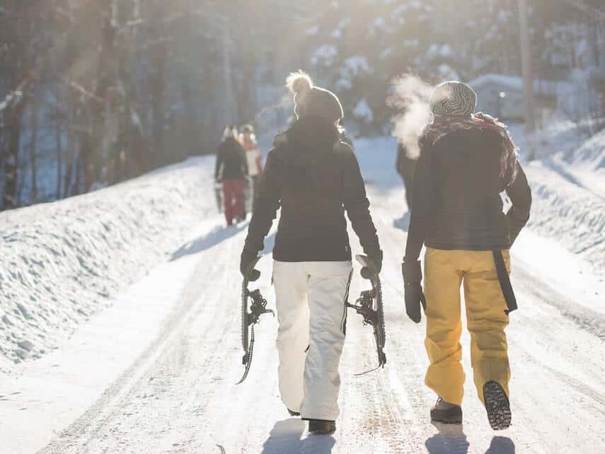 Charlottes Pass Ski Resort NSW couple walking along a snowy road carrying skis