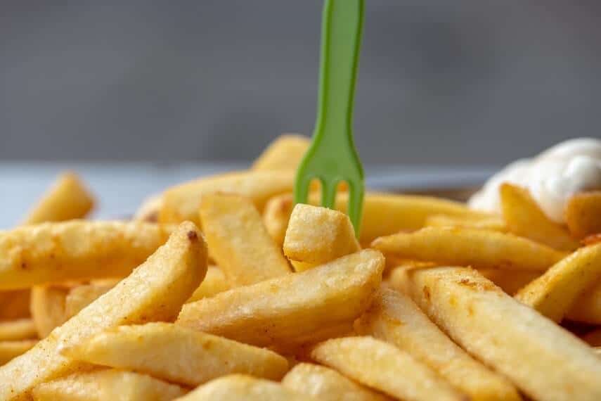 Pile of thick hot chips with a green plastic mini fork standing on top