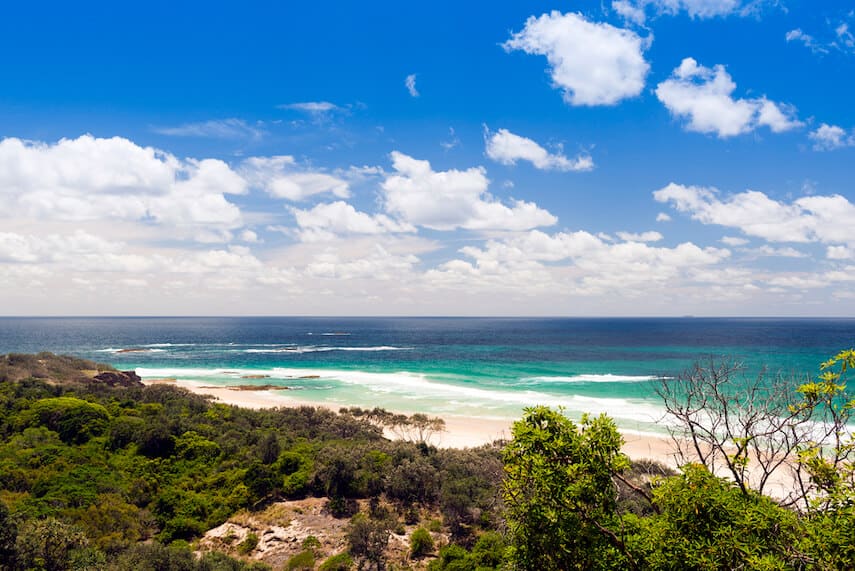 Rugged coastline of North Stradbroke Island under a bright blue sky with soft white clouds