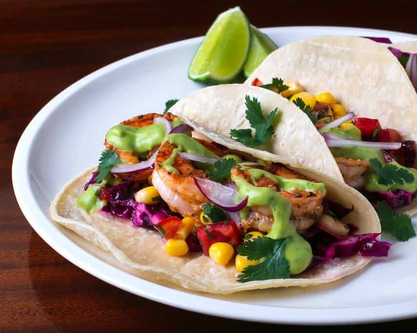 Two open soft shell tacos on a white plate with a lime wedge on the side