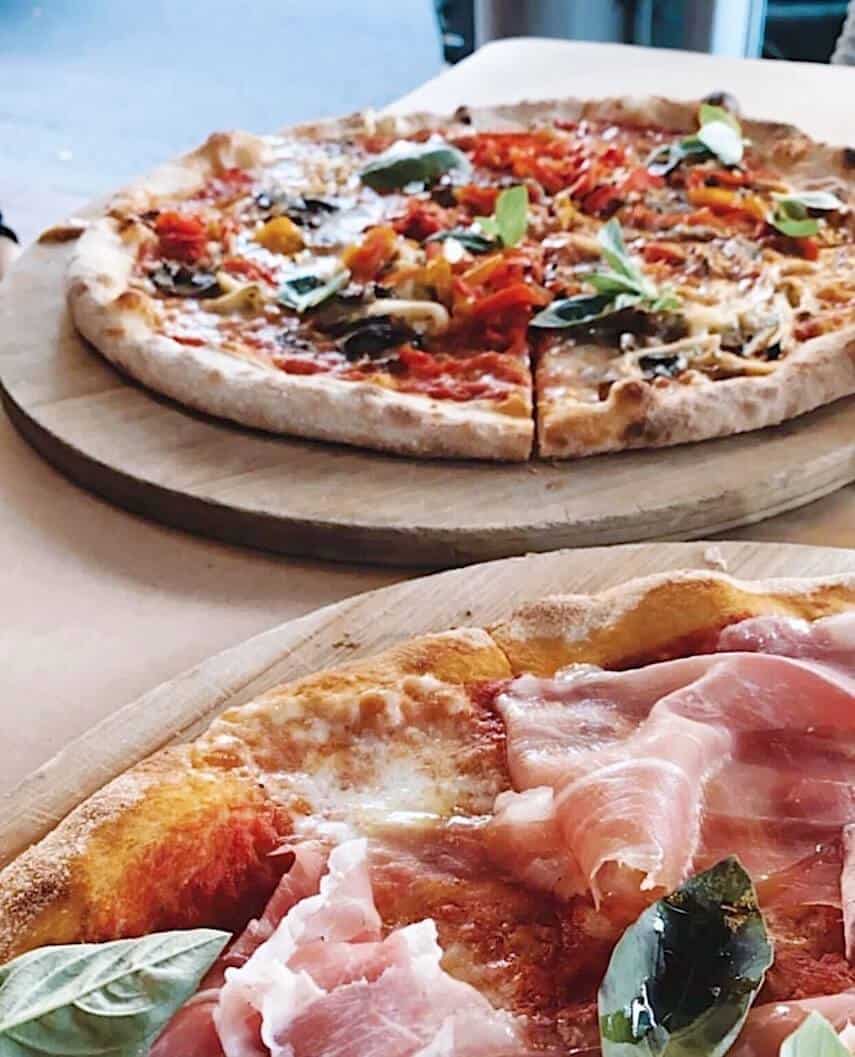 Two pizzas on wooden boards on a table