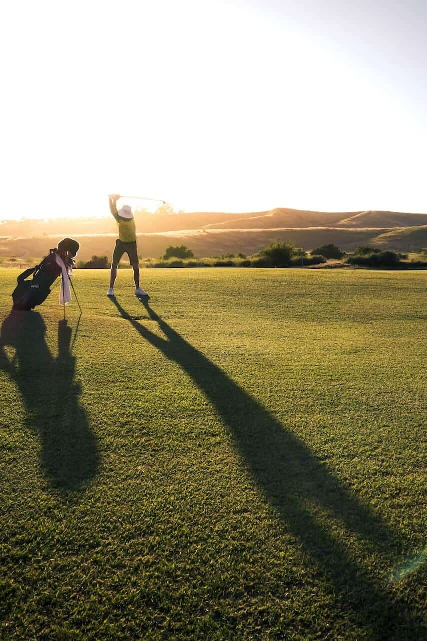 Lone golfer swinging club with sunrise in background